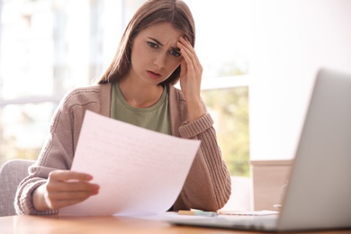 Worried woman reading letter at wooden table in room