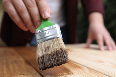 Man applying wood stain onto wooden surface against blurred background, closeup
