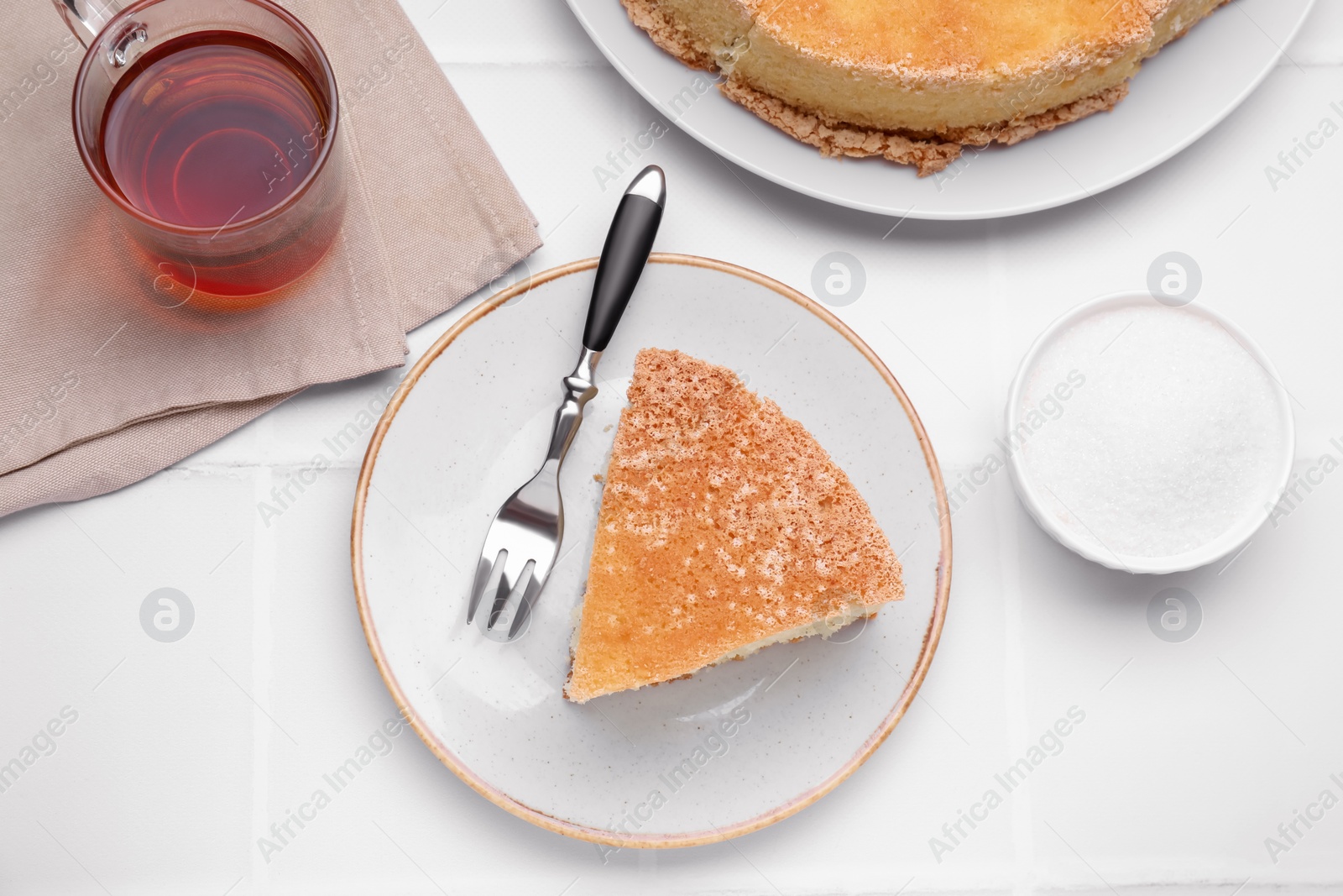 Photo of Piece of tasty sponge cake served on white tiled table, flat lay
