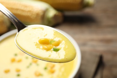 Photo of Spoon of delicious corn soup over full bowl, closeup