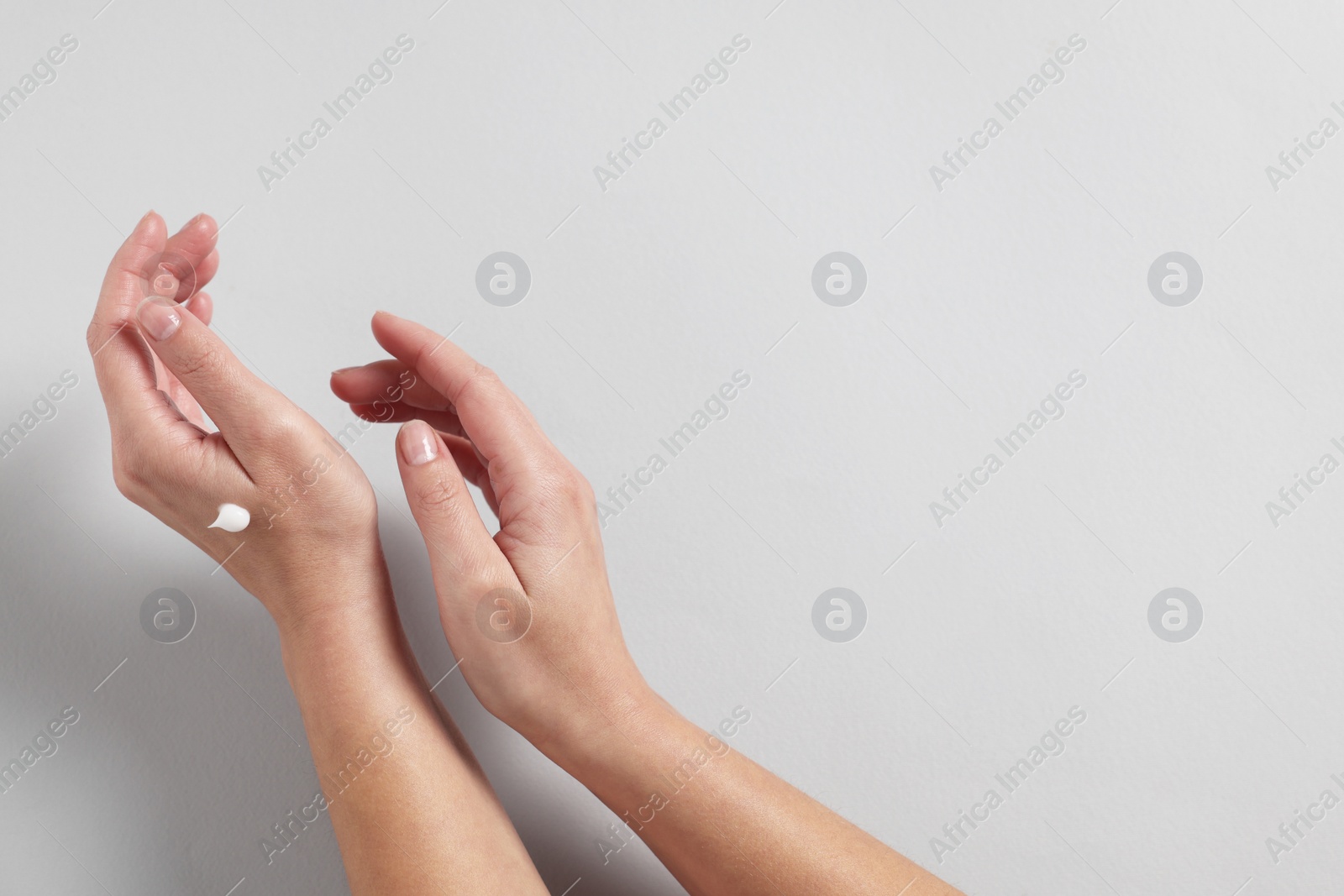 Photo of Woman with cosmetic cream on hand against light grey background, top view. Space for text