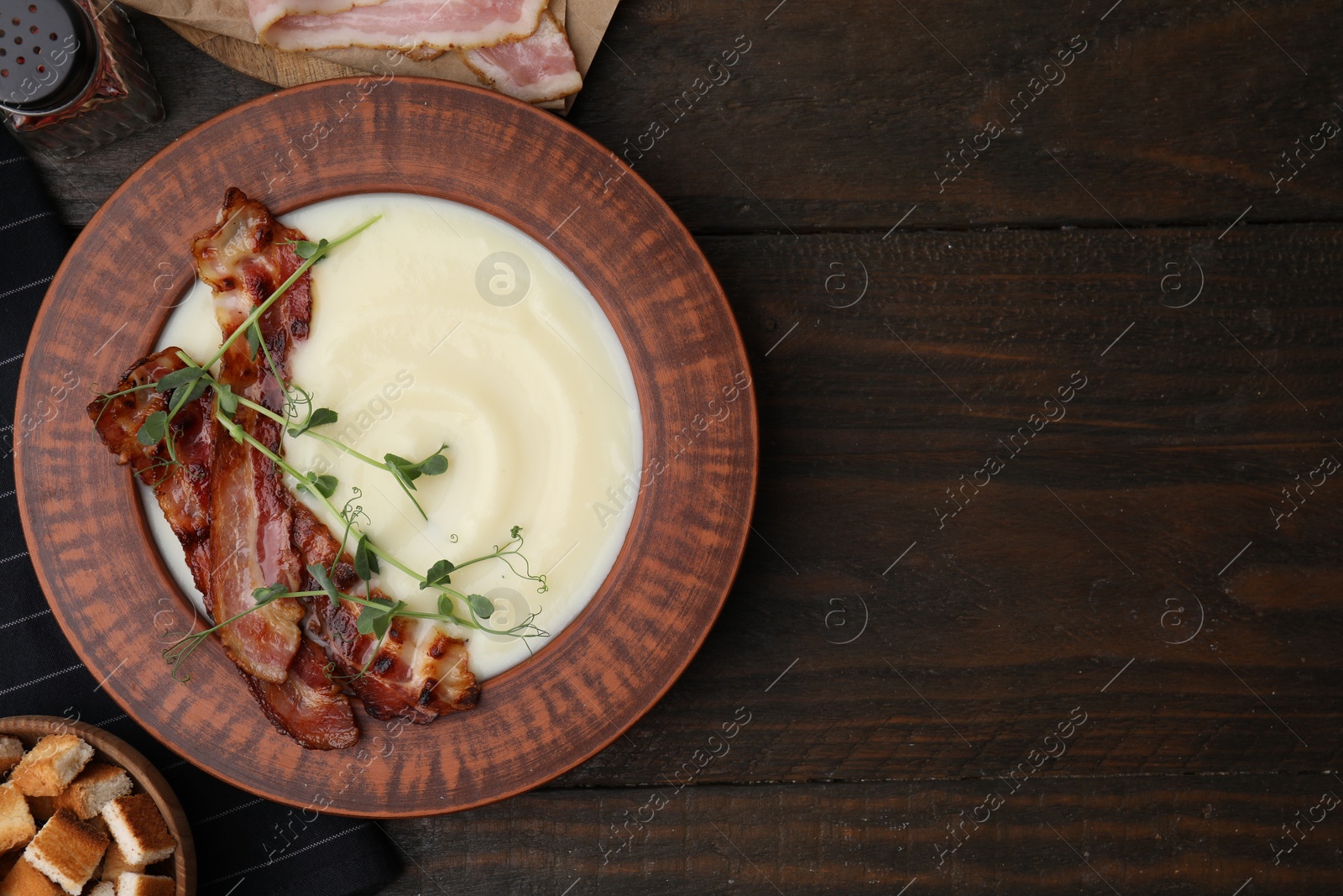 Photo of Delicious potato soup with bacon and microgreens in bowl on wooden table, flat lay. Space for text