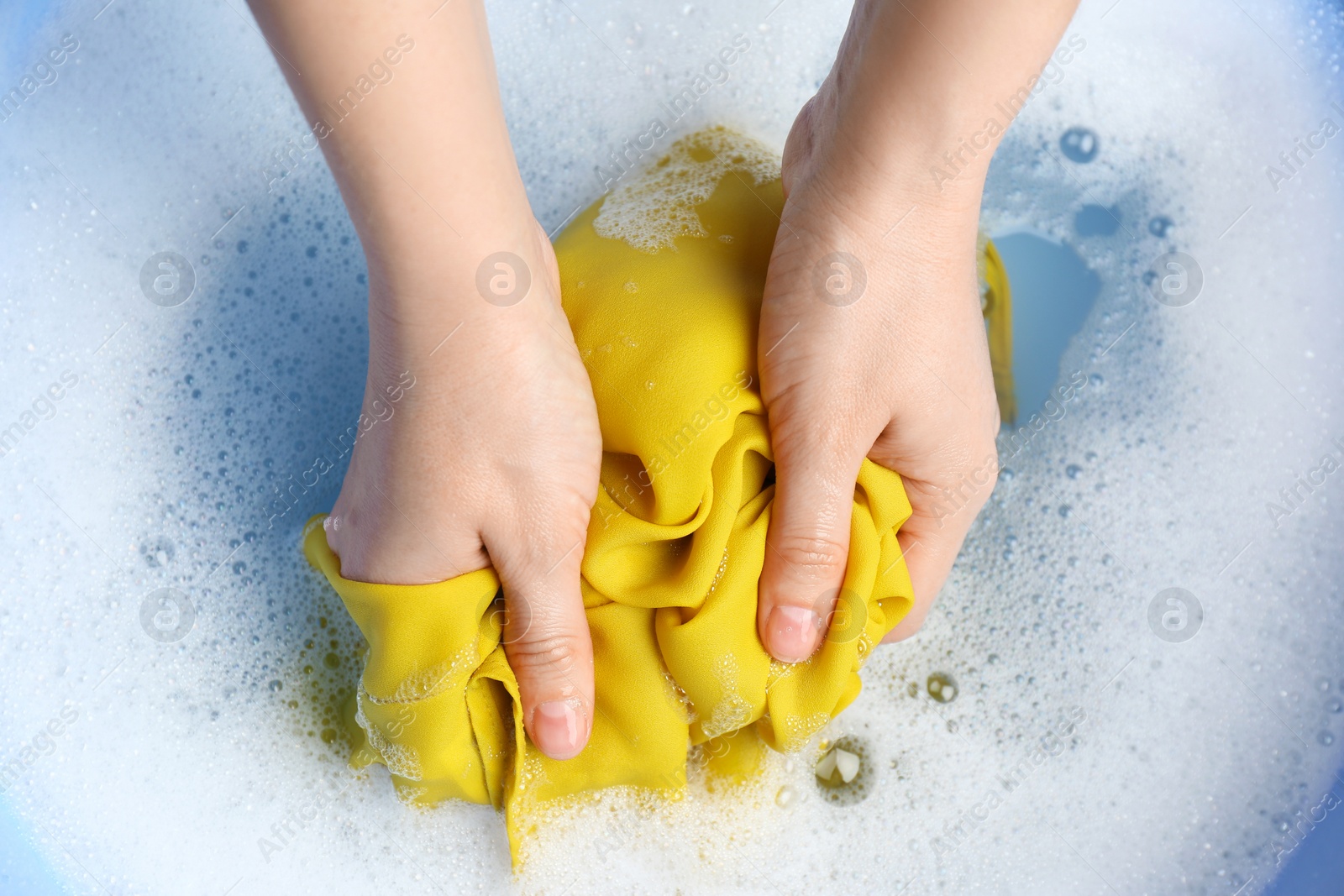 Photo of Top view of woman hand washing color clothing in suds, closeup