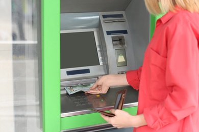 Woman taking money from cash machine outdoors, closeup