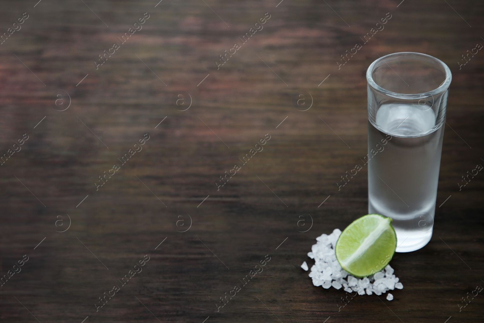 Photo of Mexican tequila shot with lime slice and salt on wooden table, space for text. Drink made from agave