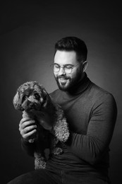 Photo of Handsome bearded man with cute dog on dark background. Black and white effect
