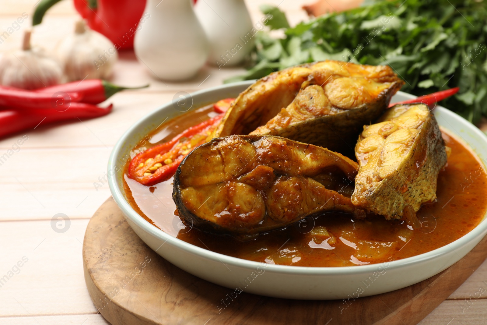 Photo of Tasty fish curry and ingredients on white wooden table, closeup. Indian cuisine