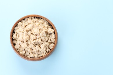 Photo of Tasty boiled oatmeal in bowl on light blue background, top view. Space for text