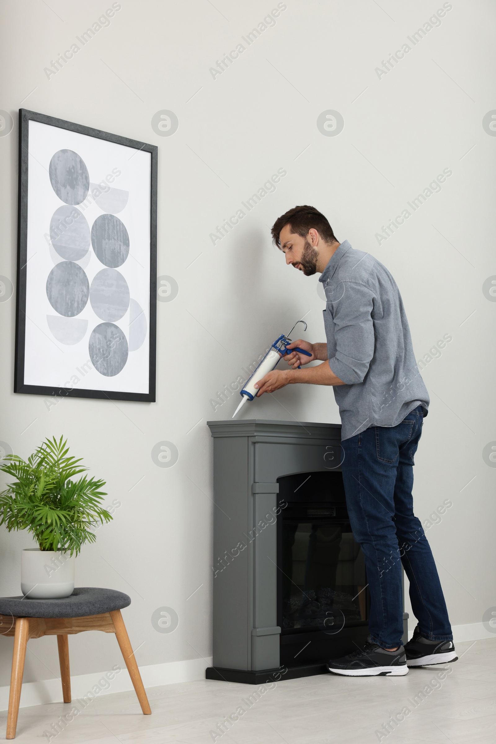 Photo of Man sealing electric fireplace with caulk near wall in room