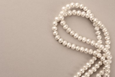 Photo of Elegant pearl necklace on beige background, top view. Space for text