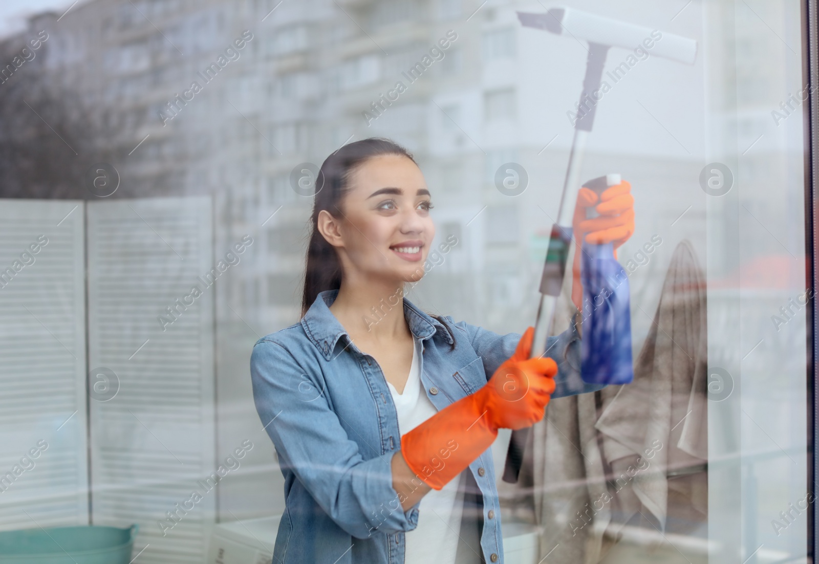 Photo of Young woman cleaning window glass at home