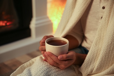 Photo of Man covered with white plaid enjoying cup of tea at fireplace, closeup
