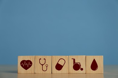 Cubes with different icons on wooden table against light blue background, space for text. Insurance concept