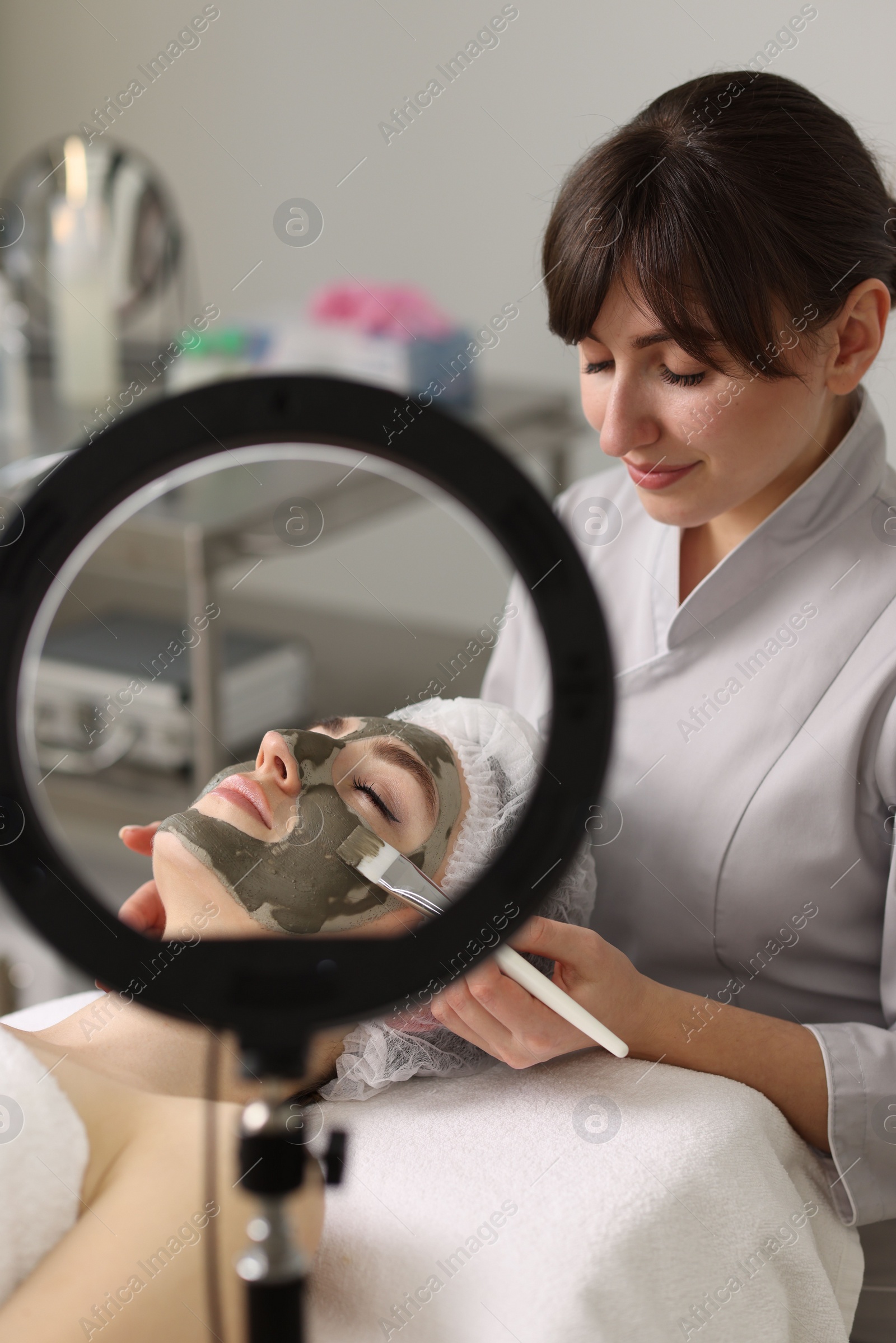 Photo of Cosmetologist applying mask on woman's face in clinic