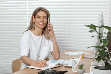 Photo of Professional accountant talking on phone while working at wooden desk in office