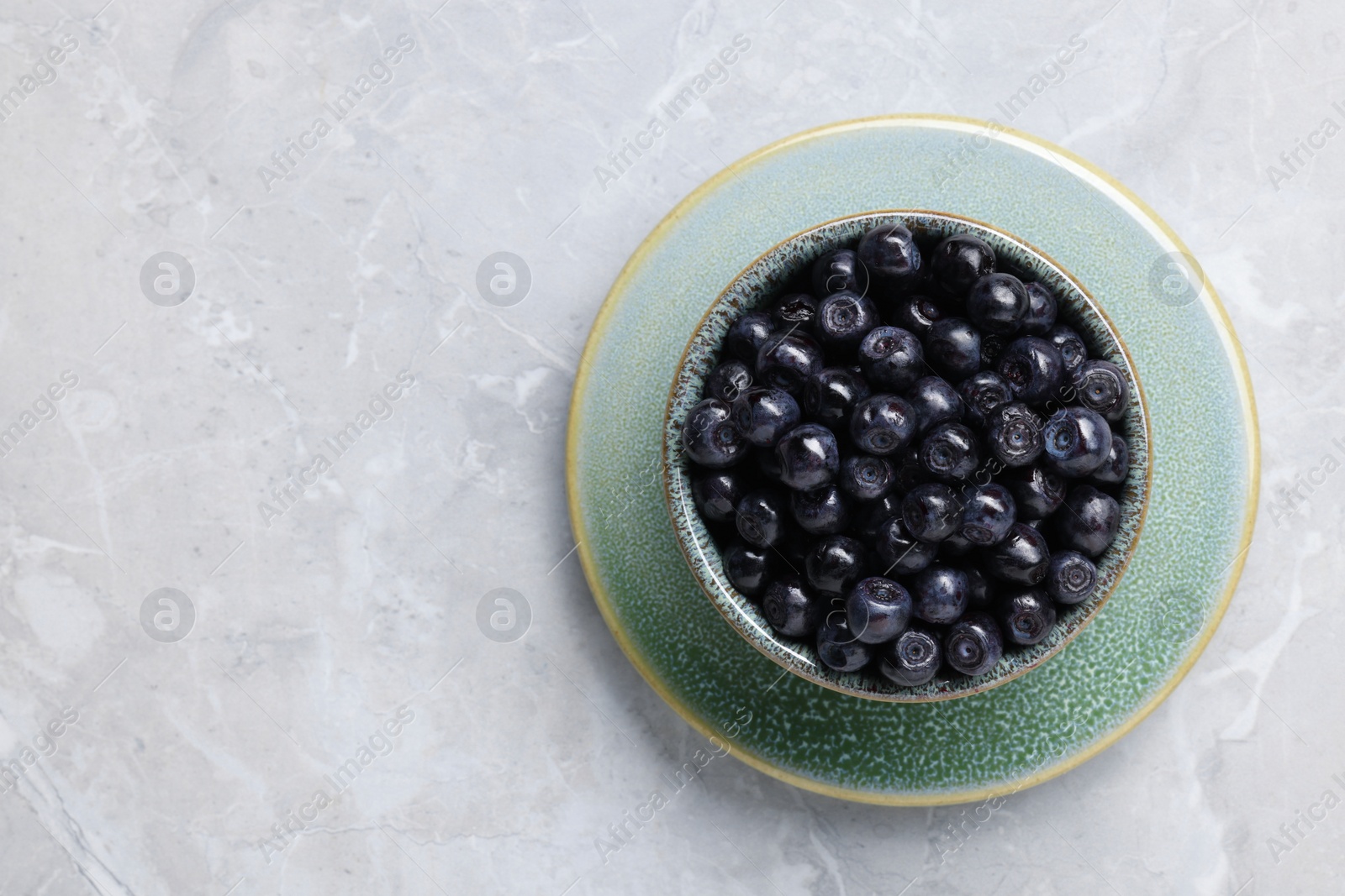 Photo of Tasty fresh bilberries in bowl on light grey marble table, top view. Space for text