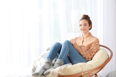 Photo of Beautiful teenage girl in warm cozy sweater sitting near window at home. space for text