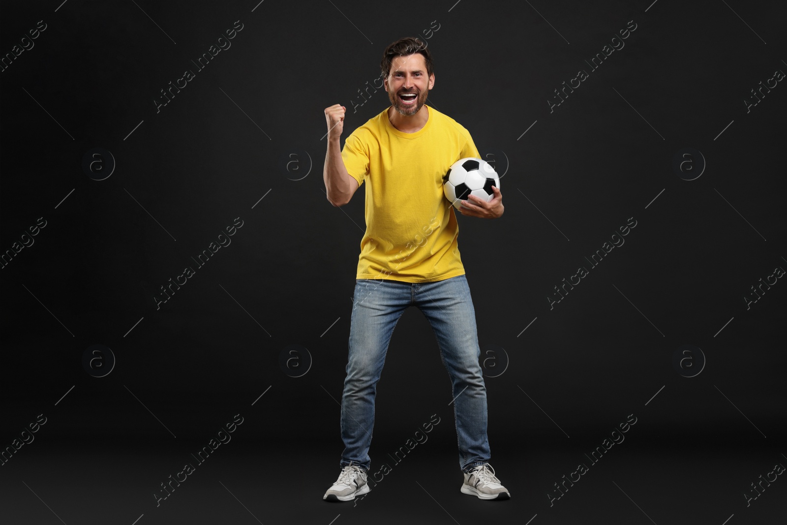 Photo of Emotional sports fan with soccer ball on black background