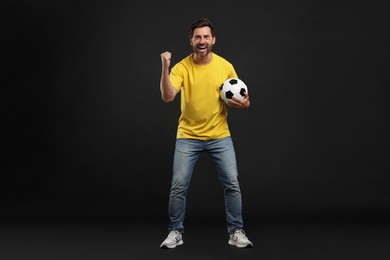 Photo of Emotional sports fan with soccer ball on black background