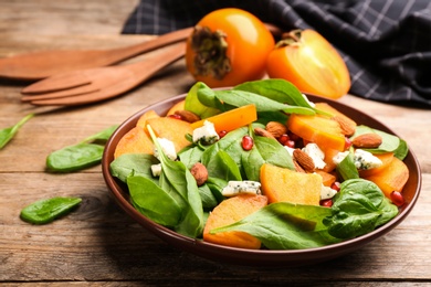 Photo of Delicious persimmon salad served on wooden table, closeup