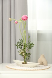 Photo of Ikebana art. Beautiful flowers and green branches carrying cozy atmosphere at home