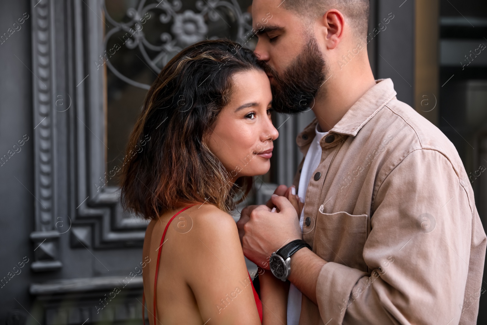 Photo of Handsome young man kissing his beautiful girlfriend near door outdoors