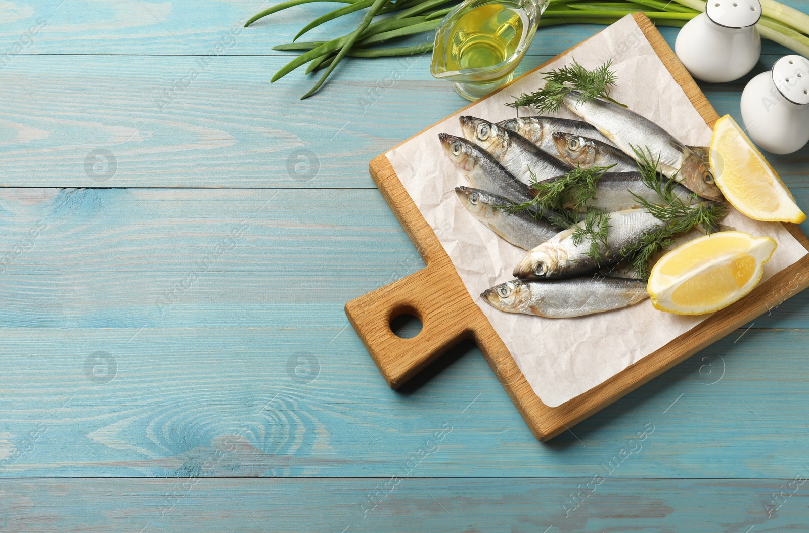 Photo of Fresh raw sprats, dill, oil and cut lemon on light blue wooden table, flat lay. Space for text