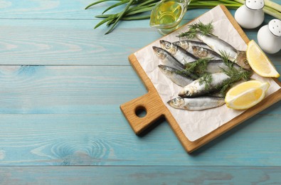 Fresh raw sprats, dill, oil and cut lemon on light blue wooden table, flat lay. Space for text