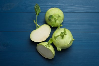 Photo of Whole and cut kohlrabi plants on blue wooden table, flat lay