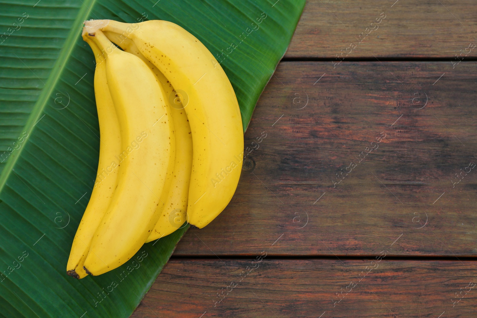 Photo of Delicious bananas and green leaf on wooden table, top view. Space for text