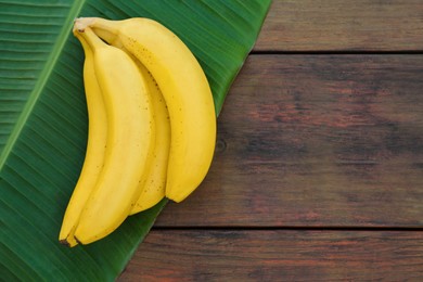 Delicious bananas and green leaf on wooden table, top view. Space for text