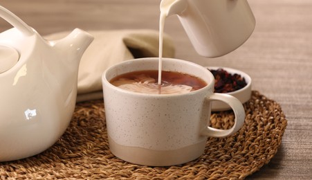 Photo of Pouring milk into cup with aromatic tea at wooden table, closeup