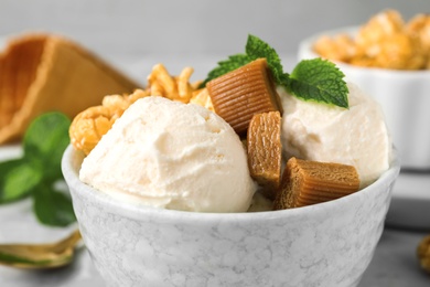 Bowl of delicious ice cream with caramel candies, popcorn and mint on table, closeup