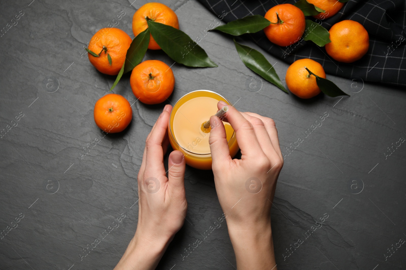 Photo of Woman with glass of fresh tangerine juice at black table, top view