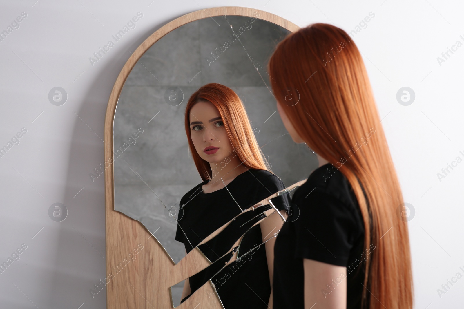 Photo of Mental problems. Depressed young woman looking at herself in broken mirror indoors