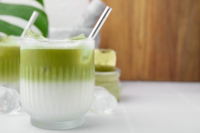 Photo of Glasses of tasty iced matcha latte on white tiled table, closeup. Space for text