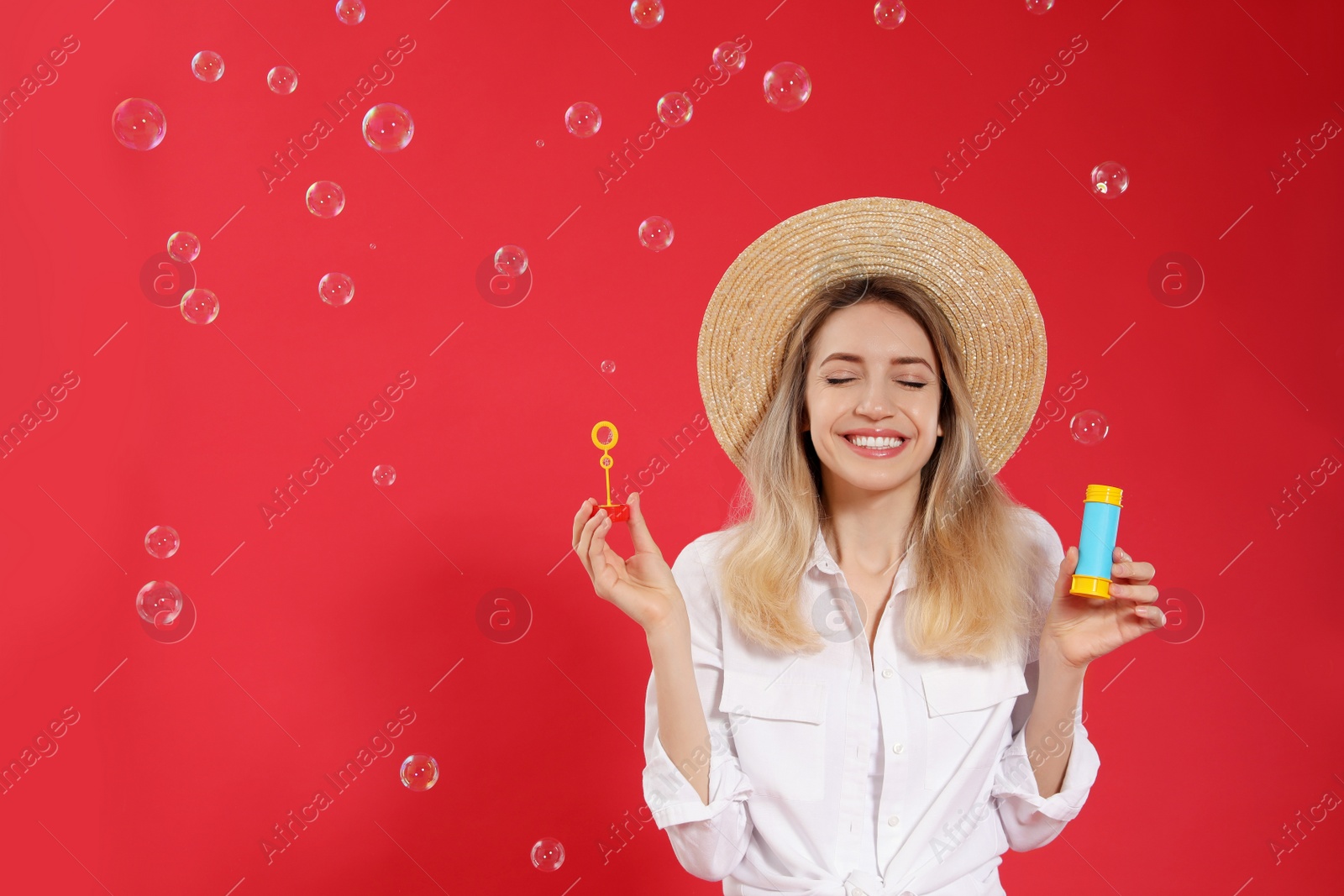 Photo of Young woman blowing soap bubbles on red background, space for text