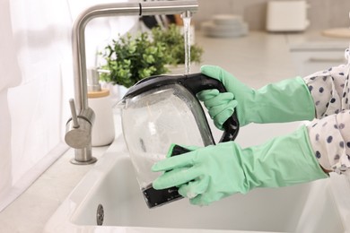 Woman washing electric kettle with sponge at sink in kitchen, closeup