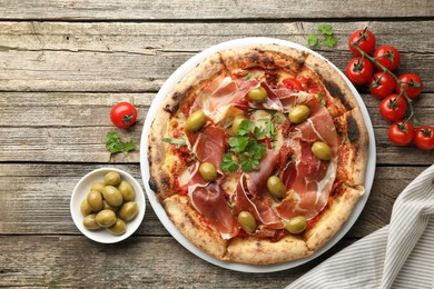 Photo of Tasty pizza with cured ham, olives, tomatoes and parsley on wooden table, top view