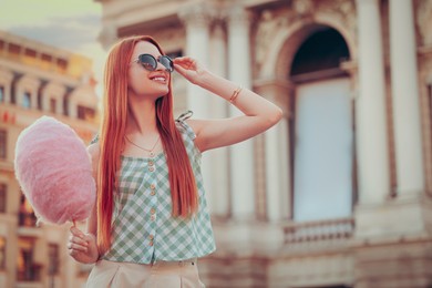 Smiling woman with cotton candy in city on sunny day. Space for text