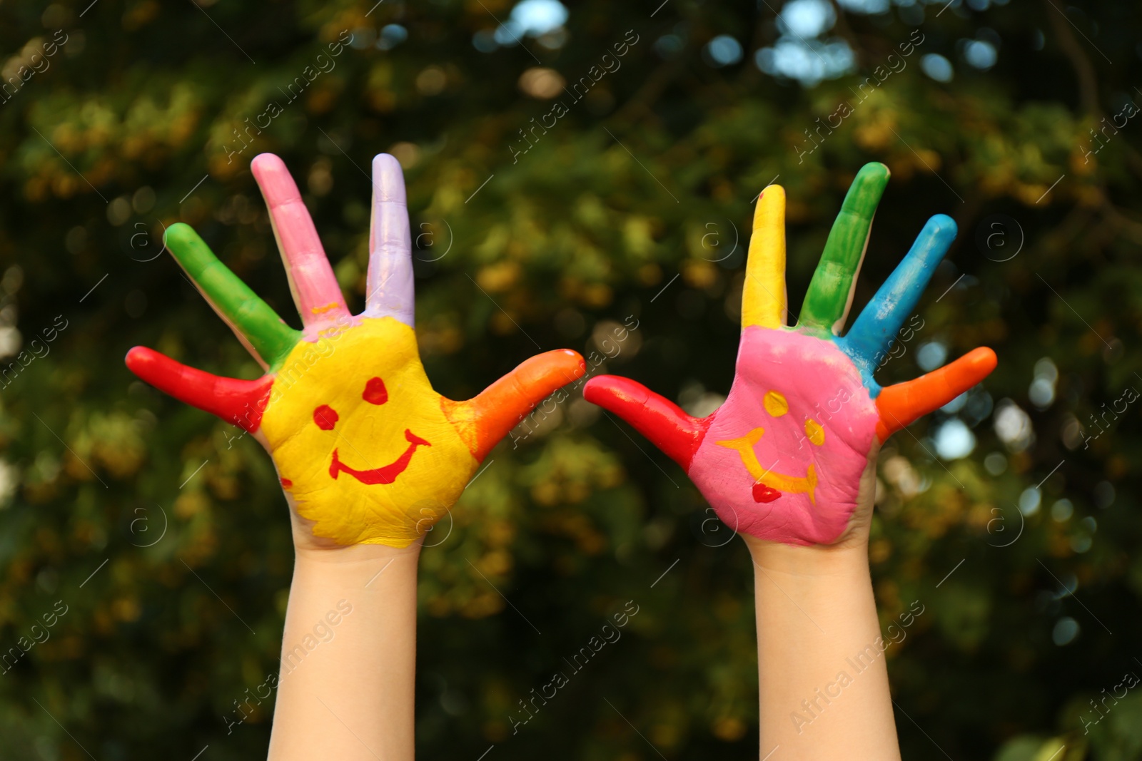 Photo of Kid with smiling face drawn on palms in green park, closeup