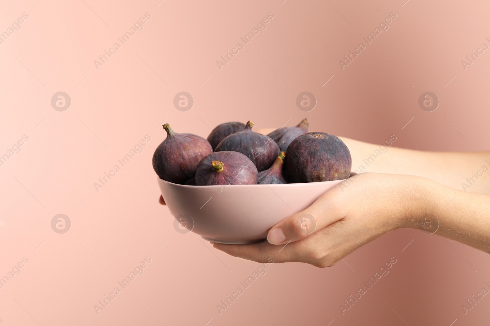 Photo of Woman holding bowl with tasty raw figs on pink  background, closeup