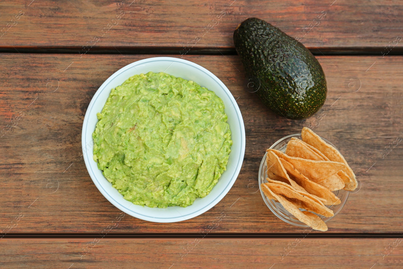 Photo of Delicious guacamole, avocado and nachos on wooden table, flat lay