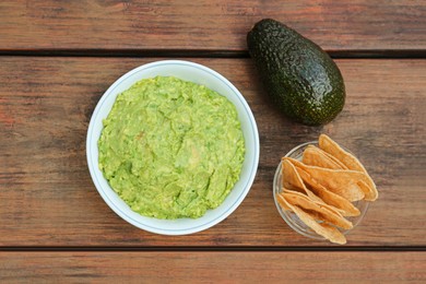 Photo of Delicious guacamole, avocado and nachos on wooden table, flat lay