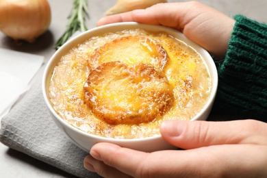 Woman with bowl of tasty homemade french onion soup at grey table, closeup