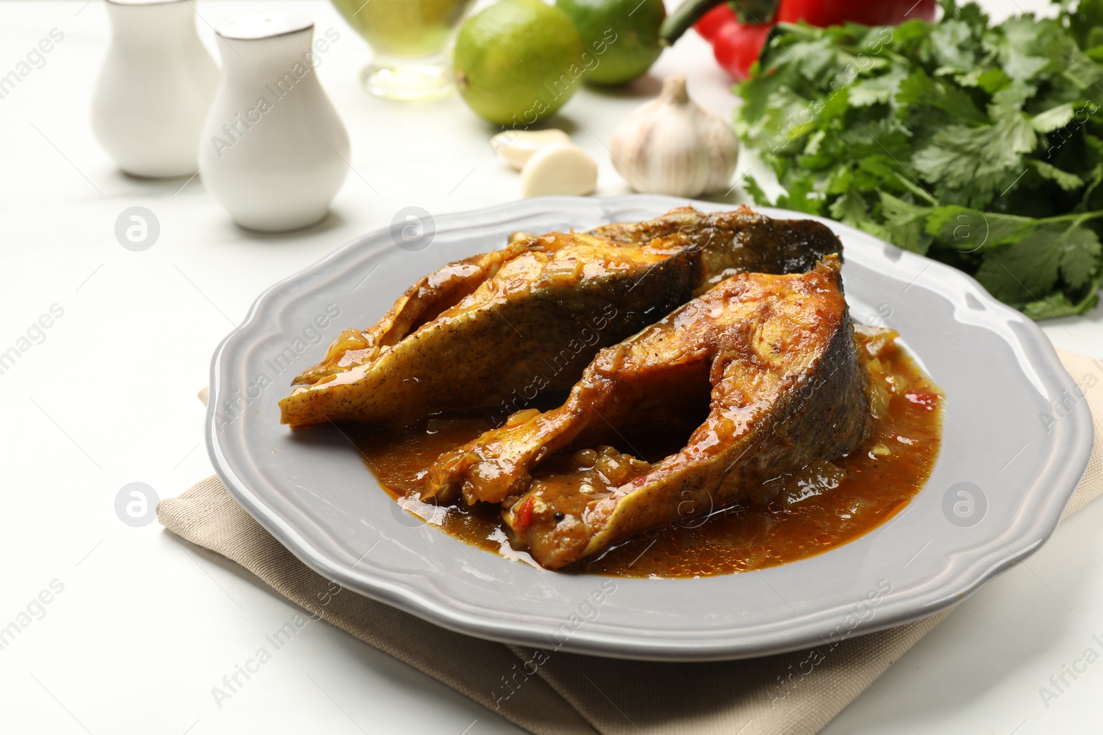 Photo of Tasty fish curry and ingredients on white table, closeup. Indian cuisine