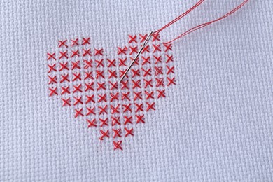 Photo of Embroidered red heart and needle on white cloth, top view