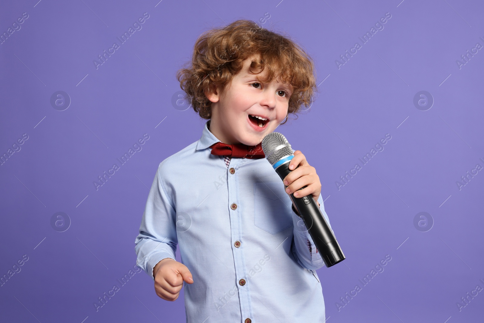 Photo of Cute little boy with microphone singing on violet background