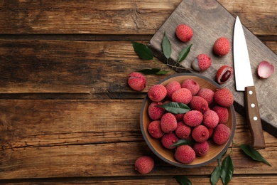 Photo of Fresh ripe lychee fruits and knife on wooden table, flat lay. Space for text