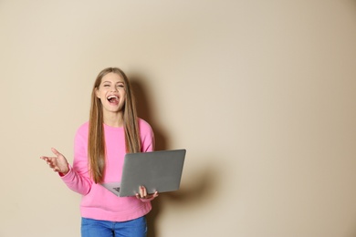 Emotional young woman with laptop celebrating victory on color background. Space for text